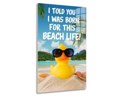 A yellow rubber duck wearing sunglasses sits on a beach, with the text "I told you I was born for this beach life!" against a backdrop of palm trees, mountains, and the ocean.
